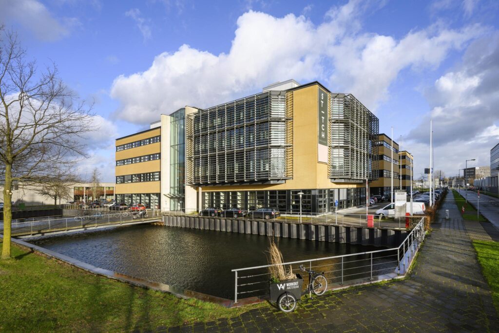 Modern kantoorgebouw aan de H.J.E. Wenckebachweg in Amsterdam met waterpartij en bakfiets op de voorgrond.